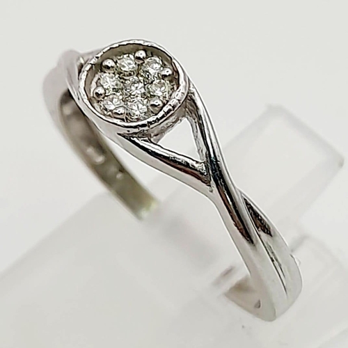 785 - A 9K White Gold Diamond Ring. Seven diamonds in a circular shape. Twists on the shoulders. Size O/N.... 