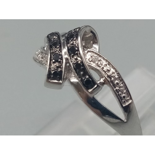 499 - A 9K White Gold Double-Crossover Diamond Ring in a Bow design - With Black and White Diamonds. Size ... 