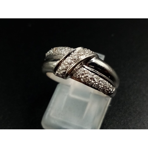 1003 - An 18K White Gold Diamond Cluster Crossover Ring.
Size O. 5.69g.