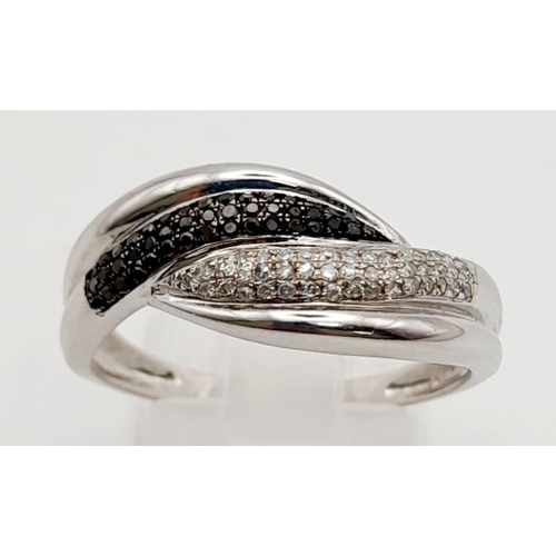 1171 - An 18K White Gold Diamond Crossover Ring. White and black diamonds. Size S. 3.2g total weight.