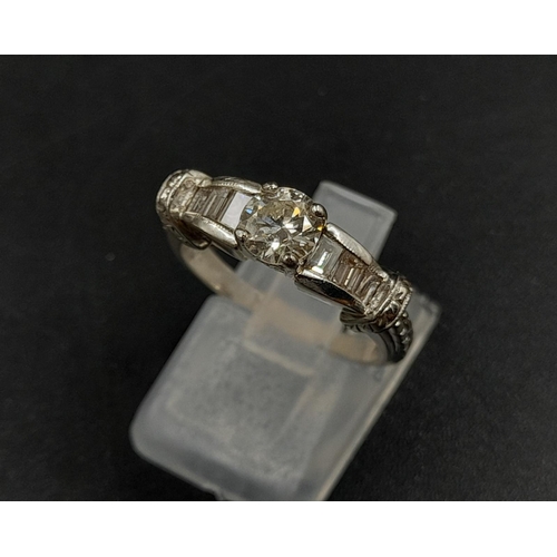 410 - A Platinum Diamond Ring - Central stone with small baguette-cut diamonds on shoulders. Size M. 7.86g