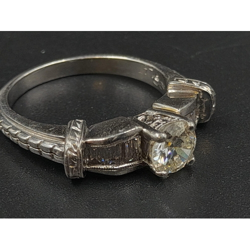 410 - A Platinum Diamond Ring - Central stone with small baguette-cut diamonds on shoulders. Size M. 7.86g