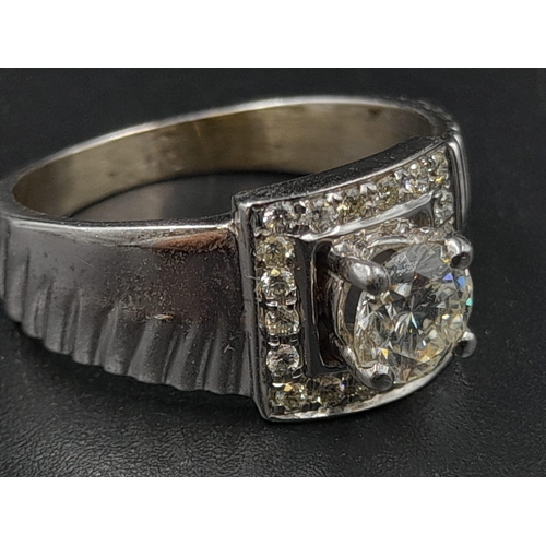 1370 - A 9K White Gold Belt-Buckle Diamond Ring. Central stone surrounded by a square belt-buckle of diamon... 