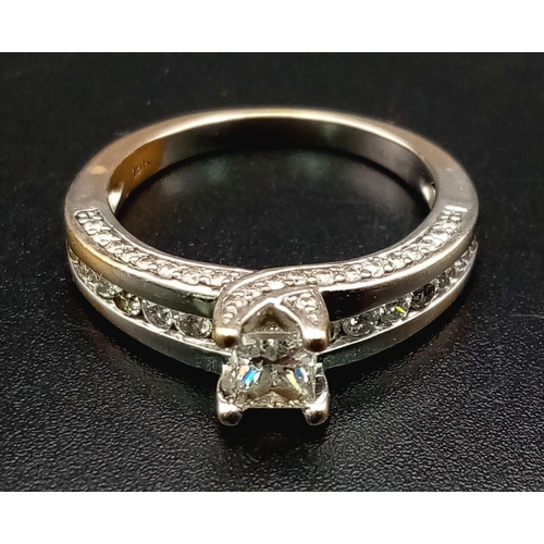 871 - An 18K White Gold Diamond Ring. Princess cut central diamond with further compliments of diamonds on... 