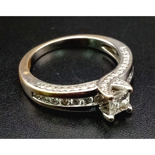 871 - An 18K White Gold Diamond Ring. Princess cut central diamond with further compliments of diamonds on... 