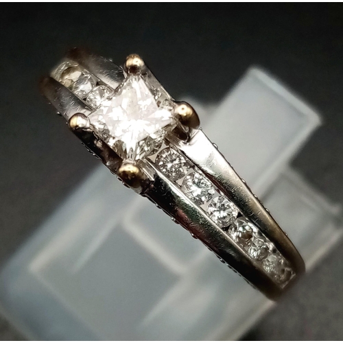 871 - An 18K White Gold Diamond Ring. Princess cut central diamond with further compliments of diamonds on... 