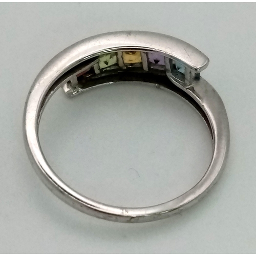 921 - A 9K white gold ring in a cross over design with five gemstones (aquamarine, amethyst, citrine, peri... 