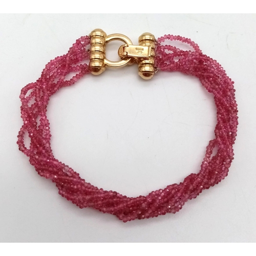 396 - An 18K Gold, Diamond and Ruby Four Strand Bracelet. Four twisted strands of pink rubies with a gold ... 