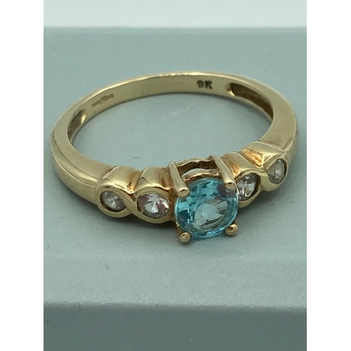 455 - 9k GOLD RING, having Blue Topaz coloured stone mounted to top with WHITE TOPAZ gemstones set to shou... 