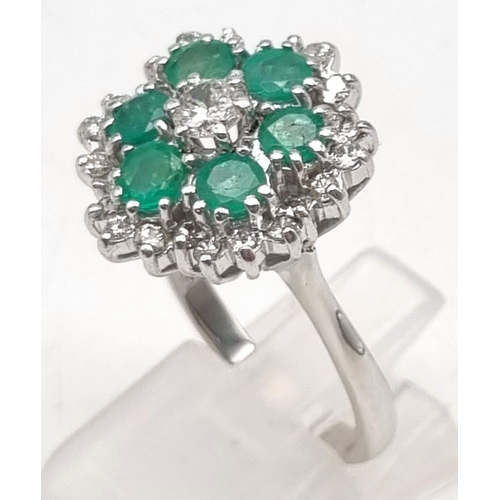 12 - A Very Pretty 18K White Gold, Emerald and Diamond Ring. Floral design with a central diamond, six em... 
