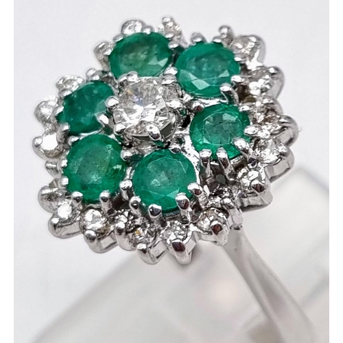 12 - A Very Pretty 18K White Gold, Emerald and Diamond Ring. Floral design with a central diamond, six em... 