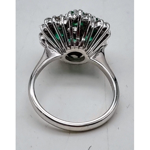 12 - A Very Pretty 18K White Gold, Emerald and Diamond Ring. Floral design with a central diamond, six em... 