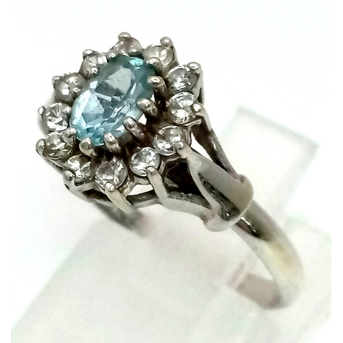 480 - A 9K White Gold and Blue Topaz Ring. Central oval topaz with a CZ surround. Size L. 2.59g total weig... 