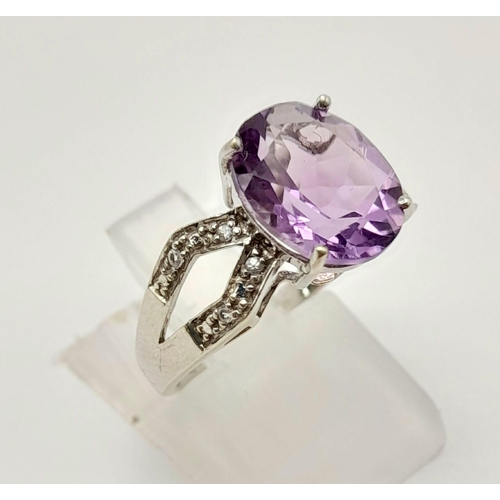 1438 - A 9K White Gold Amethyst and Diamond Ring. Central clean oval amethyst with wings of diamond decorat... 