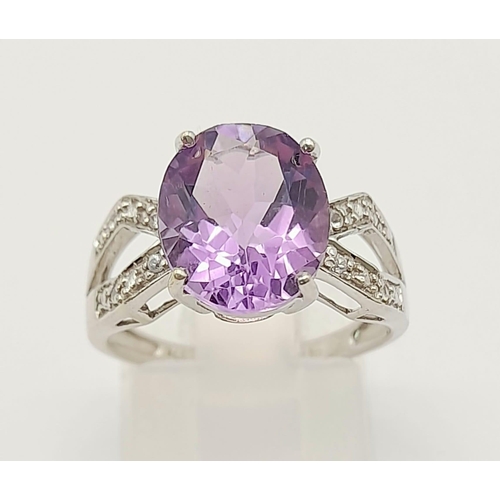 1438 - A 9K White Gold Amethyst and Diamond Ring. Central clean oval amethyst with wings of diamond decorat... 