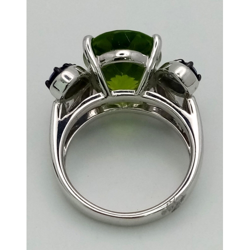 152 - A very attractive, platinum ring with a large, oval cut peridot, surrounded by eight, round cut tanz... 