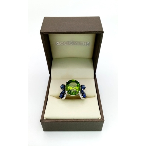 152 - A very attractive, platinum ring with a large, oval cut peridot, surrounded by eight, round cut tanz... 