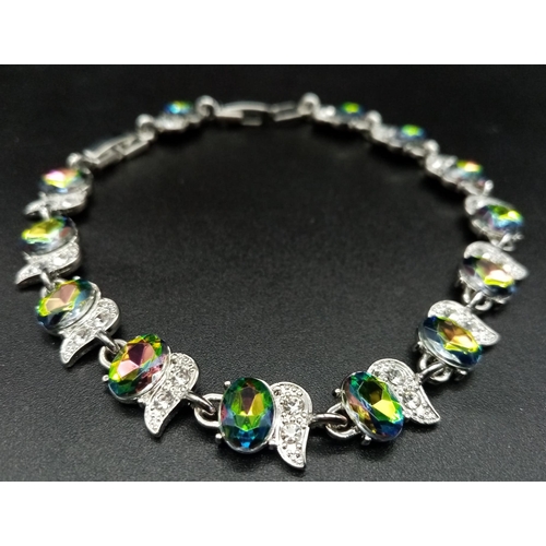 1276 - A Mystic Topaz Tennis Bracelet. Spare link attached. Set in white metal. 19cm