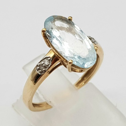 1036 - A 9K Yellow Gold Blue Gemstone and Diamond Ring. Elongated central oval stone with two small diamond... 