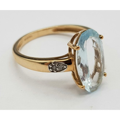 1036 - A 9K Yellow Gold Blue Gemstone and Diamond Ring. Elongated central oval stone with two small diamond... 