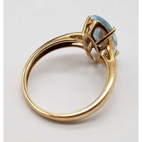 1036 - A 9K Yellow Gold Blue Gemstone and Diamond Ring. Elongated central oval stone with two small diamond... 