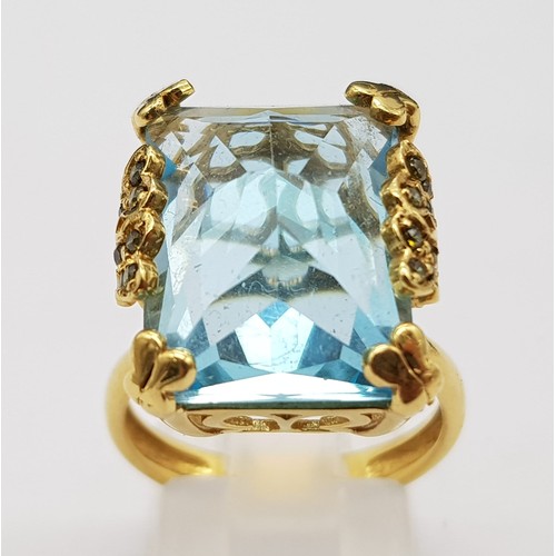 359 - An 18K Yellow Gold Blue Topaz Ring. Pale blue 10ct stone in a scroll setting. 8.81g total weight. Si... 