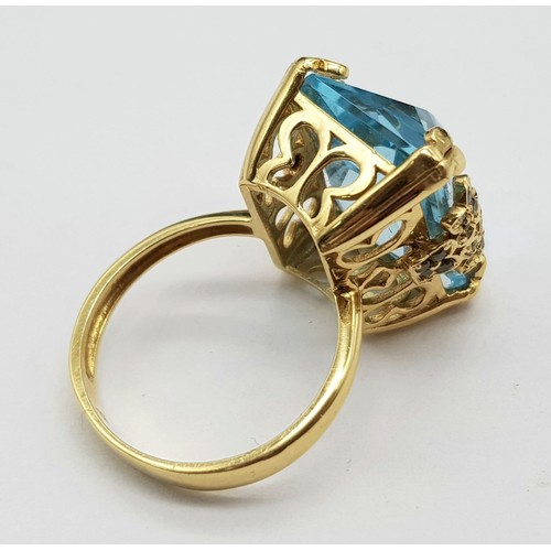 359 - An 18K Yellow Gold Blue Topaz Ring. Pale blue 10ct stone in a scroll setting. 8.81g total weight. Si... 