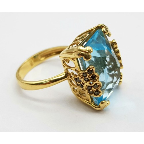 359 - An 18K Yellow Gold Blue Topaz Ring. Pale blue 10ct stone in a scroll setting. 8.81g total weight. Si... 