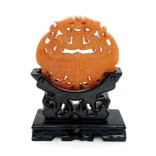 740 - An antique, Chinese, hand carved orange jade amulet on a custom made wooden carved base. The amulet ... 