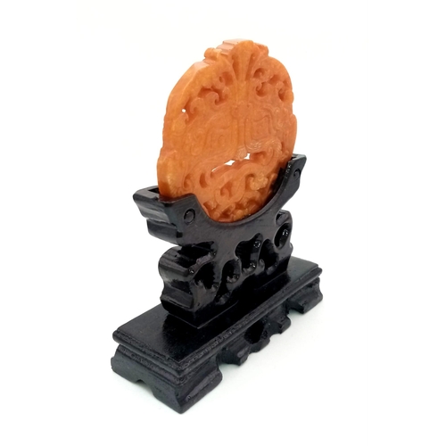 740 - An antique, Chinese, hand carved orange jade amulet on a custom made wooden carved base. The amulet ... 