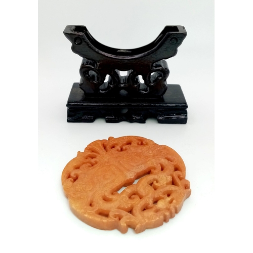 740 - An antique, Chinese, hand carved orange jade amulet on a custom made wooden carved base. The amulet ... 