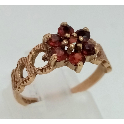 1290 - A Vintage 9K Yellow Gold Garnet Love Ring. Floral garnet central design with heart decoration either... 