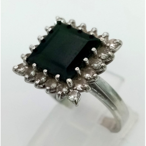 45 - An 18K White Gold Emerald and Diamond Ring. Square-cut dark green emerald with a white diamond surro... 