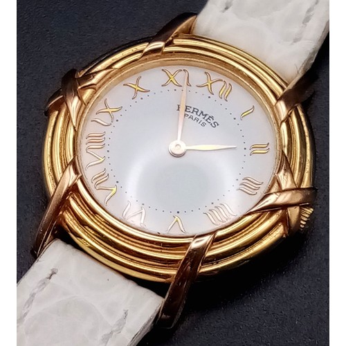 123 - A HERMES 18K GOLD LADIES WRISTWATCH WITH DESIGNER BEZEL, WHITE DIAL , ROMAN NUMERALS ON A WHITE LEAT... 