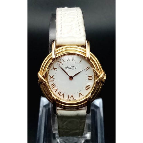 123 - A HERMES 18K GOLD LADIES WRISTWATCH WITH DESIGNER BEZEL, WHITE DIAL , ROMAN NUMERALS ON A WHITE LEAT... 