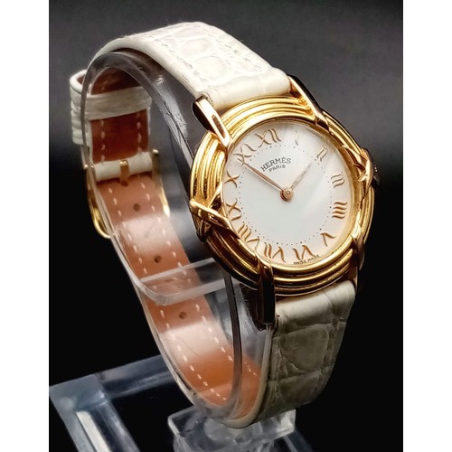 123 - A HERMES 18K GOLD LADIES WRISTWATCH WITH DESIGNER BEZEL, WHITE DIAL , ROMAN NUMERALS ON A WHITE LEAT... 