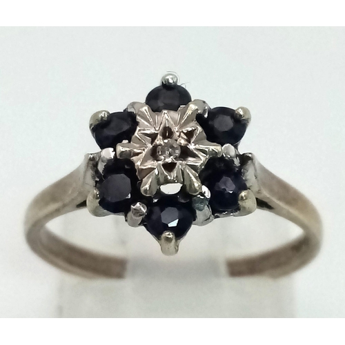 871 - A 9K White Gold Sapphire and Diamond Ring. Six sapphires with a small central diamond. Size M. 2.64g... 