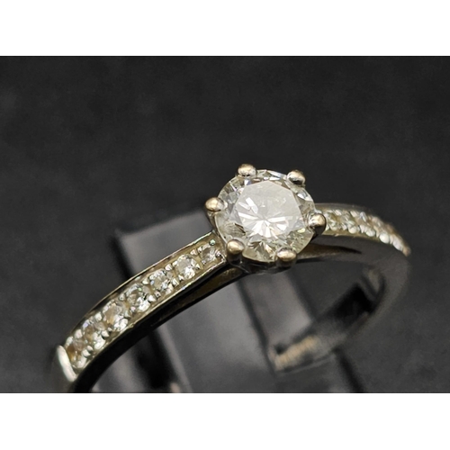 188 - An 18 K white gold ring with a brilliant cut diamond and more diamonds on the shoulders of the ring.... 