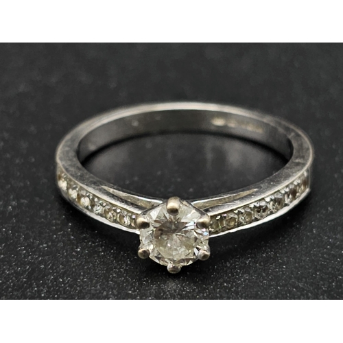 188 - An 18 K white gold ring with a brilliant cut diamond and more diamonds on the shoulders of the ring.... 