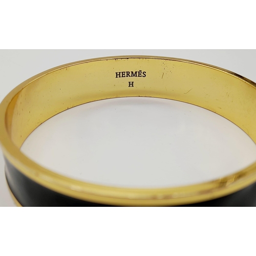 325 - A Hermes Gold Plated Bangle. Logo on inner and outer black enamel. 6.5cm inner diameter.