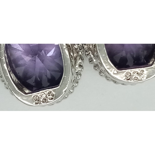 912 - A New Pair of Sterling Silver Crown Mounted Amethyst Set Secure Stud Earrings. Set with 14mm Oval Cu... 