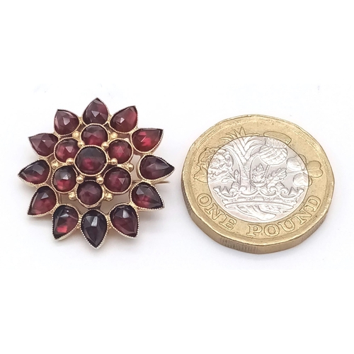 296 - AN 18K GOLD FLORAL DESIGN BROOCH WITH DARK RED RUBY STONES .  4.1gms   2.4cms diameter