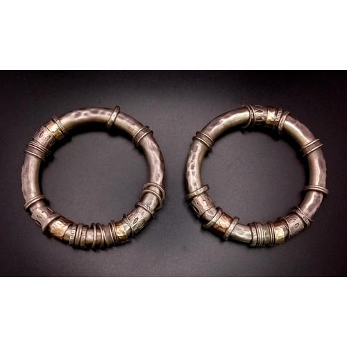 73 - A pair of silver and gold bangles in tubular form with loose ring decoration. The bangles have a pie... 