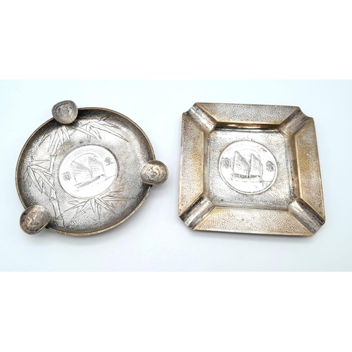 211 - 2 CHINESE SILVER VINTAGE ASH TRAYS WITH COINS EMBEDDED IN THE BASE.    160gms