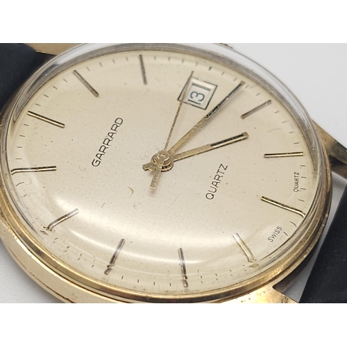 276 - A Vintage 9K Gold Garrard Gents Quartz Watch. Black leather strap. 9K Gold case - 34mm. Cream dial w... 