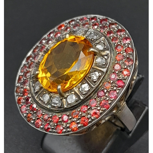 264 - A Citrine, Ruby and Diamond Ring. Rich, central oval cut citrine with a diamond and double ruby halo... 