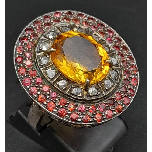 264 - A Citrine, Ruby and Diamond Ring. Rich, central oval cut citrine with a diamond and double ruby halo... 