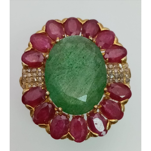 898 - An Emerald & Ruby Gilded Ring. Oval cut. Oval cut emerald with a halo of rubies with diamond accents... 