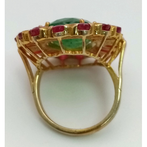 898 - An Emerald & Ruby Gilded Ring. Oval cut. Oval cut emerald with a halo of rubies with diamond accents... 