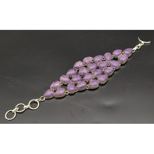 230 - A glorious, white metal (untested), bracelet with numerous, oval charoite cabochons. In a presentati... 